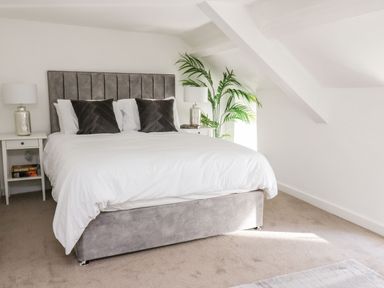 A bedroom with a double bed with gray headboard and white bedding two bedside tables with lamps and a green plant at Lane Cottage in Cardigan