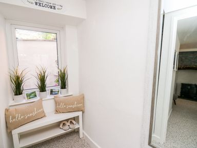 A small corner with a white bench with two hello sunshine cushions and three potted plants on a windowsill at Lane Cottage in Cardigan