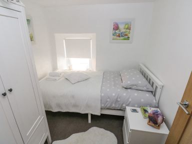 A small bedroom with a single bed with polka dot bedding a white wardrobe a bedside table and a small window at Lane Cottage in Cardigan