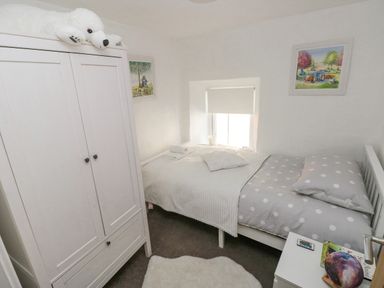 A small bedroom with a single bed with polka dot bedding a white wardrobe with a stuffed polar bear on top a small bedside table with books and a decorative item two framed pictures on the walls at Lane Cottage in Cardigan