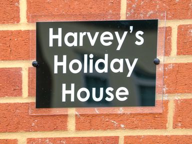 A black sign with white text reading Harveys Holiday House mounted on a red brick wall at Harveys Holiday House in Hunstanton