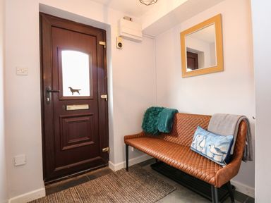 An entryway with a brown door with a dog silhouette on the window and a brown bench with cushions and a mirror on the wall at Harveys Holiday House in Hunstanton