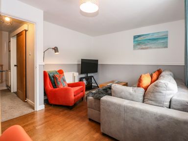 A living room with a gray sofa and an orange armchair a wooden floor and a painting on the wall at Harveys Holiday House in Hunstanton