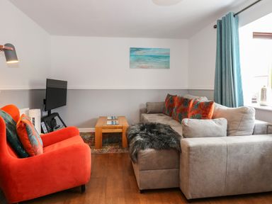 A living room with a gray sofa and orange armchair a wooden coffee table and a wall-mounted TV at Harveys Holiday House in Hunstanton