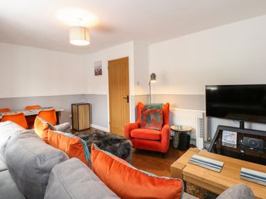 A living room with grey sofa and orange cushions dining table with orange chairs and a red armchair at Harveys Holiday House in Hunstanton