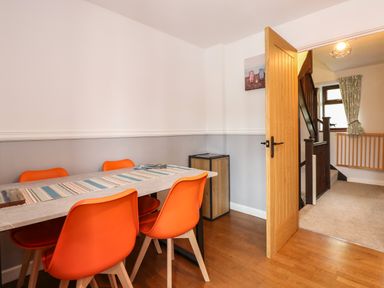 A dining area with a table and four orange chairs next to an open door showing a staircase at Harveys Holiday House in Hunstanton