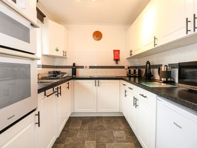 A kitchen with white cabinets black countertops microwave stove and small appliances at Harveys Holiday House in Hunstanton
