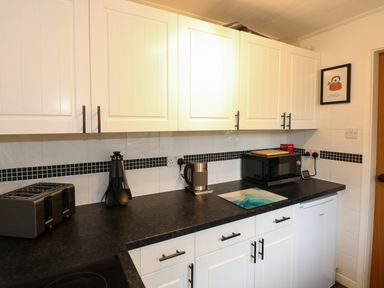 A kitchen countertop with a toaster kettle microwave utensils and cabinets at Harveys Holiday House in Hunstanton