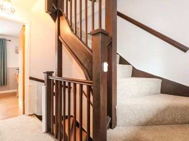 A carpeted staircase with dark wood railing and a hallway leading to a room with a wooden floor at Harveys Holiday House in Hunstanton