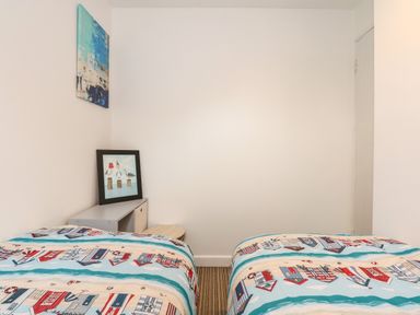 A bedroom with two single beds with patterned bedding a small cabinet with a framed picture and a painting on the wall at Harveys Holiday House in Hunstanton