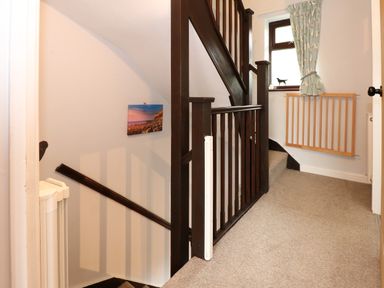 A hallway with stairs brown railing a window with a curtain and a baby gate at Harvey's Holiday House in Hunstanton