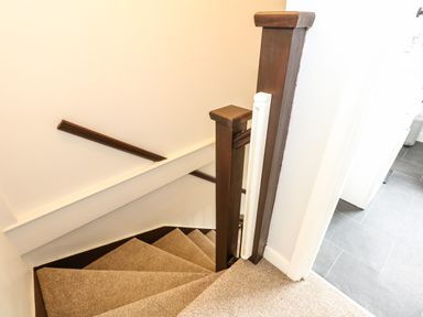A carpeted staircase with wooden railing and white walls adjacent to a tiled floor room at Harveys Holiday House in Hunstanton