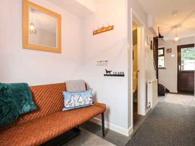 An entryway with a brown bench with pillows a coat rack a mirror a staircase and a wooden door at Harveys Holiday House in Hunstanton