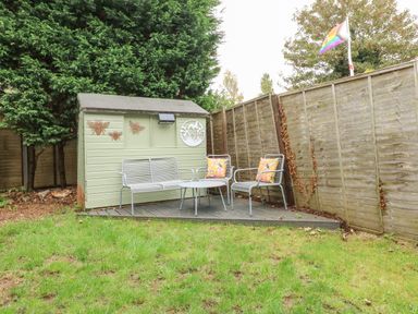 A garden area with a small green shed metal chairs and a table on a wooden deck with cushions on the chairs at Harveys Holiday House in Hunstanton