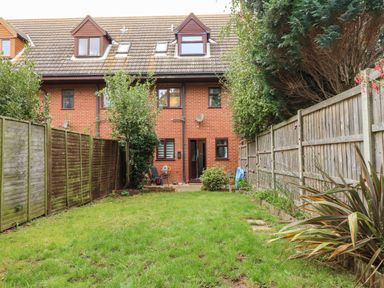A backyard with grass and plants surrounded by wooden fences behind a brick house at Harveys Holiday House in Hunstanton