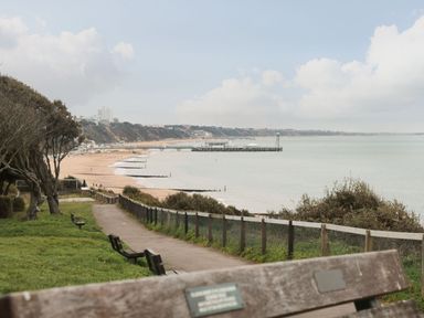 A coastal walkway with benches overlooking a sandy beach and a pier at The Anchorage in Bournemouth