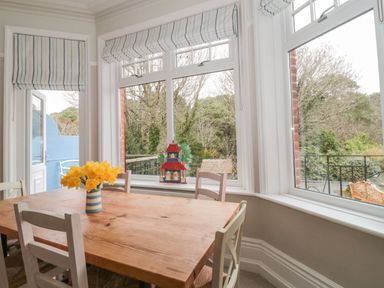 A dining area with a wooden table and white chairs near windows and a vase with yellow flowers at The Anchorage in Bournemouth