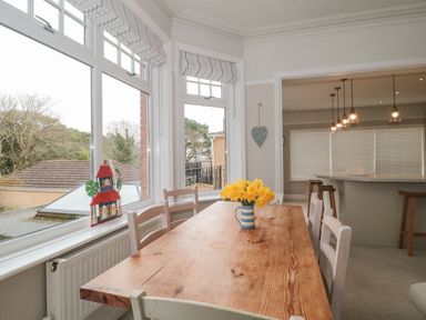 A dining area with a wooden table and chairs a vase with flowers on the table adjacent to a kitchen with bar stools at The Anchorage in Bournemouth