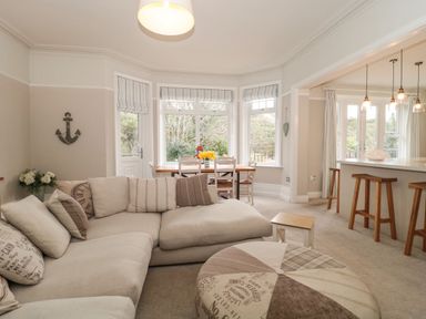 A living room with a sectional sofa near a dining table and a kitchen counter with stools at The Anchorage in Bournemouth
