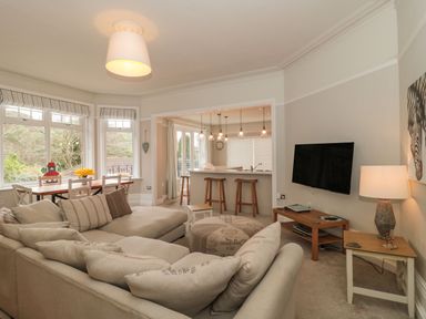 A living room with a beige sofa dining table with chairs and a wall mounted TV at The Anchorage in Bournemouth