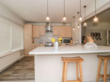 A kitchen with wooden cabinets a white countertop and wooden stools at The Anchorage in Bournemouth