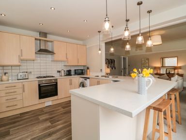 A kitchen with wooden cabinets an island with stools and pendant lights at The Anchorage in Bournemouth