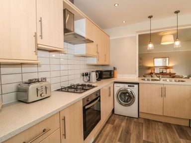 A kitchen with wooden cabinets, a gas stove, oven, toaster, washing machine, microwave, kettle, and a double sink at The Anchorage in Bournemouth