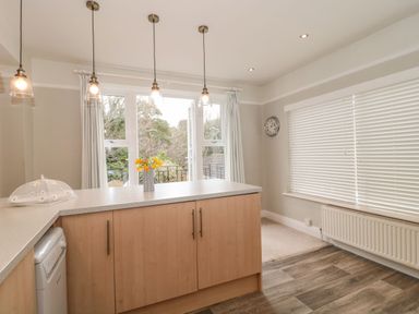 A kitchen with wooden cabinets a countertop with flowers a dishwashing machine large windows with curtains and blinds at The Anchorage in Bournemouth