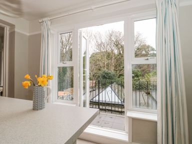 A countertop with a vase of yellow flowers next to an open balcony door with striped curtains at The Anchorage in Bournemouth