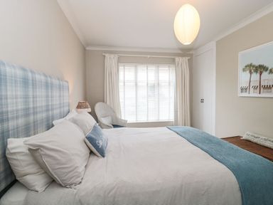A bedroom with a bed with blue and white bedding a window with curtains a chair a closet and a wall picture at The Anchorage in Bournemouth