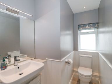 A bathroom with a white sink and mirror on the left and a toilet under a window on the right at The Anchorage in Bournemouth