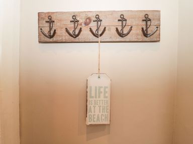 A wooden wall hook rack with five anchor-shaped hooks and a hanging sign that reads life is better at the beach