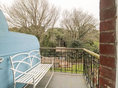 A balcony with a white metal bench black railing and a blue wall overlooking trees and a garden at The Anchorage in Bournemouth
