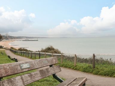 A wooden bench near a paved path overlooking a beach and sea at The Anchorage in Bournemouth