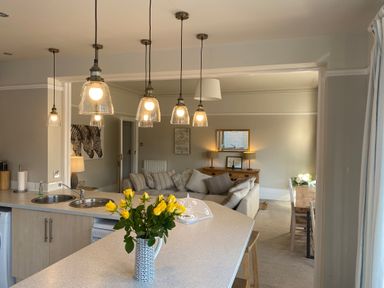 A kitchen island with a vase of yellow flowers and hanging lights overlooking a living room and dining area at The Anchorage in Bournemouth