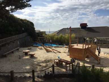 An outdoor playground with a wooden ship structure and sand area near a building with a Vesuvio sign at The Anchorage in Bournemouth