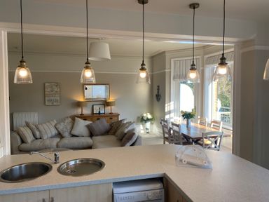 An open plan kitchen with a sink, a living area with a sofa and cushions, and a dining area with a wooden table and chairs at The Anchorage in Bournemouth