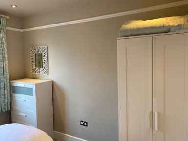 A bedroom with a white chest of drawers a wardrobe with blankets on top and patterned curtains at The Anchorage in Bournemouth