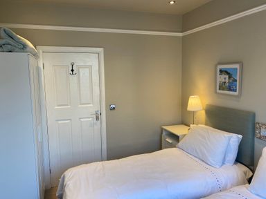 A bedroom with two single beds a bedside table with a lamp a wardrobe a door and a framed picture on the wall at The Anchorage in Bournemouth