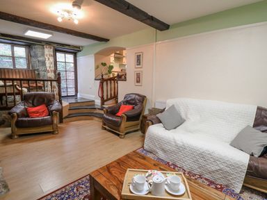 A living room with leather armchairs and a sofa covered with a white throw and a wooden coffee table with a tea set at The Searle in Nantmel near Rhayader