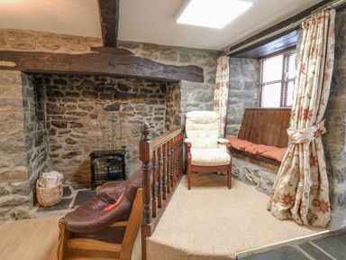 A stone walled room with a fireplace a leather armchair an upholstered armchair and a window seat with cushions at The Searle in Nantmel near Rhayader