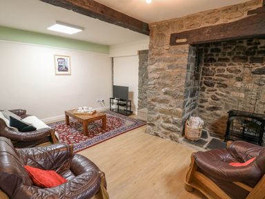 A living room with leather armchairs a wooden coffee table a decorative rug a television on a stand and a stone fireplace at The Searle in Nantmel near Rhayader