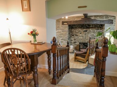 A dining area with wooden table and chairs next to a stairway leading to a stone fireplace and a brown chair at The Searle Nantmel near Rhayader