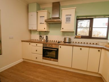 A kitchen with cream cabinets wooden floor oven and a window at The Searle in Nantmel near Rhayader
