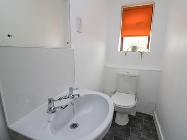 A bathroom with a sink and toilet under a window with an orange blind and a plant at The Searle in Nantmel near Rhayader