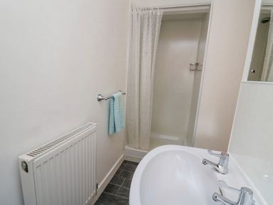 A bathroom with a white sink a shower with a curtain a towel rail with a towel and a radiator at The Searle in Nantmel near Rhayader