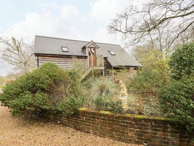 A wooden house with a staircase surrounded by bushes and a statue in a garden at Avon Turn View in Alderbury
