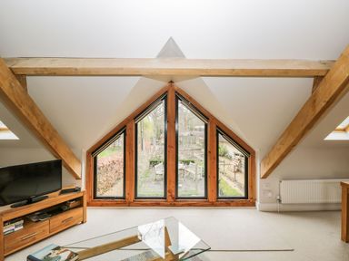 A living room with triangular windows wooden beams a television and a glass coffee table at Avon Turn View in Alderbury