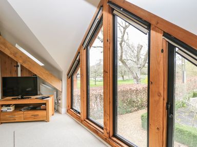 A room with large wooden framed windows a wooden TV stand with a television and books at Avon Turn View in Alderbury