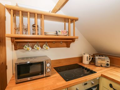 A kitchen countertop with a microwave glass stove kettle toaster and wooden shelf with cups plates bowls at Avon Turn View in Alderbury